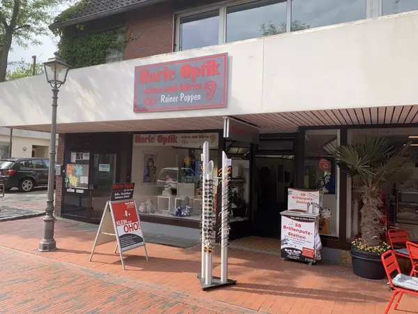 Optikergeschäft mit Brillenständer, Schaufenster und Brillenputzstation auf Gehweg.