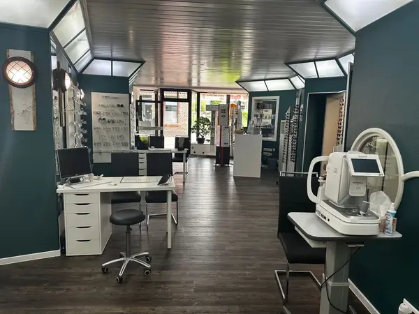 Modernes Optikergeschäft mit Brillenregalen, Beratungstischen und Sehtestgerät.